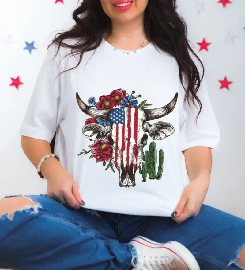 White t-shirt featuring a cow skull decorated with American flag pattern, roses, and a cactus design.