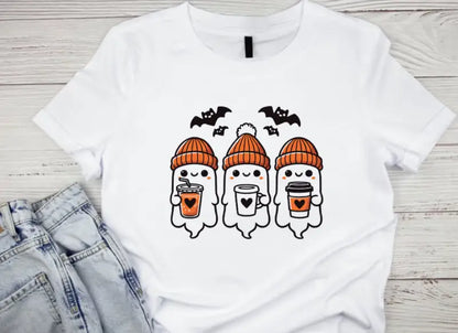 White t-shirt featuring three cute ghost characters wearing orange beanies and holding coffee cups, with black bats flying above them.