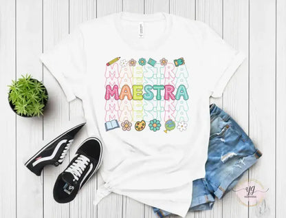 White t-shirt with colorful ’Maestra’ text and school-themed graphics printed on it.