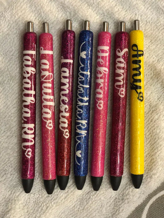 Seven glittery pens arranged in a row with pink, blue, and yellow colors.