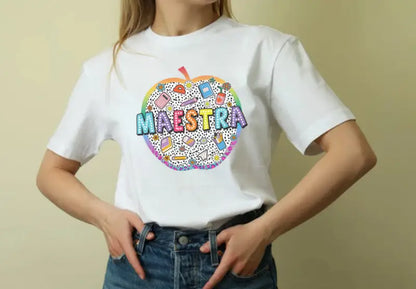 White t-shirt featuring a colorful circular apple design with ’MAESTRA’ text and educational doodles.